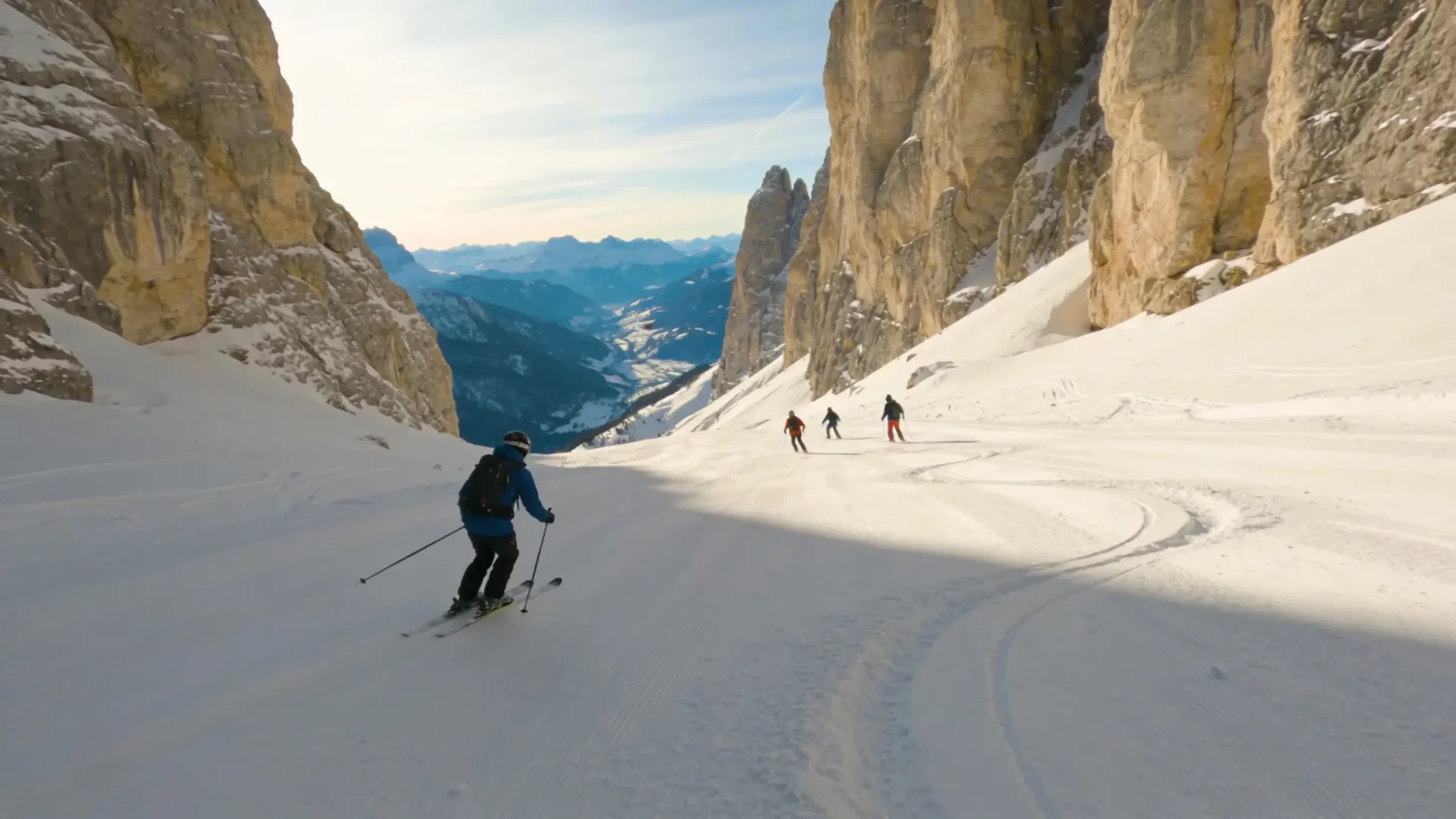 Four skiers descending a wide run between towering limestone walls