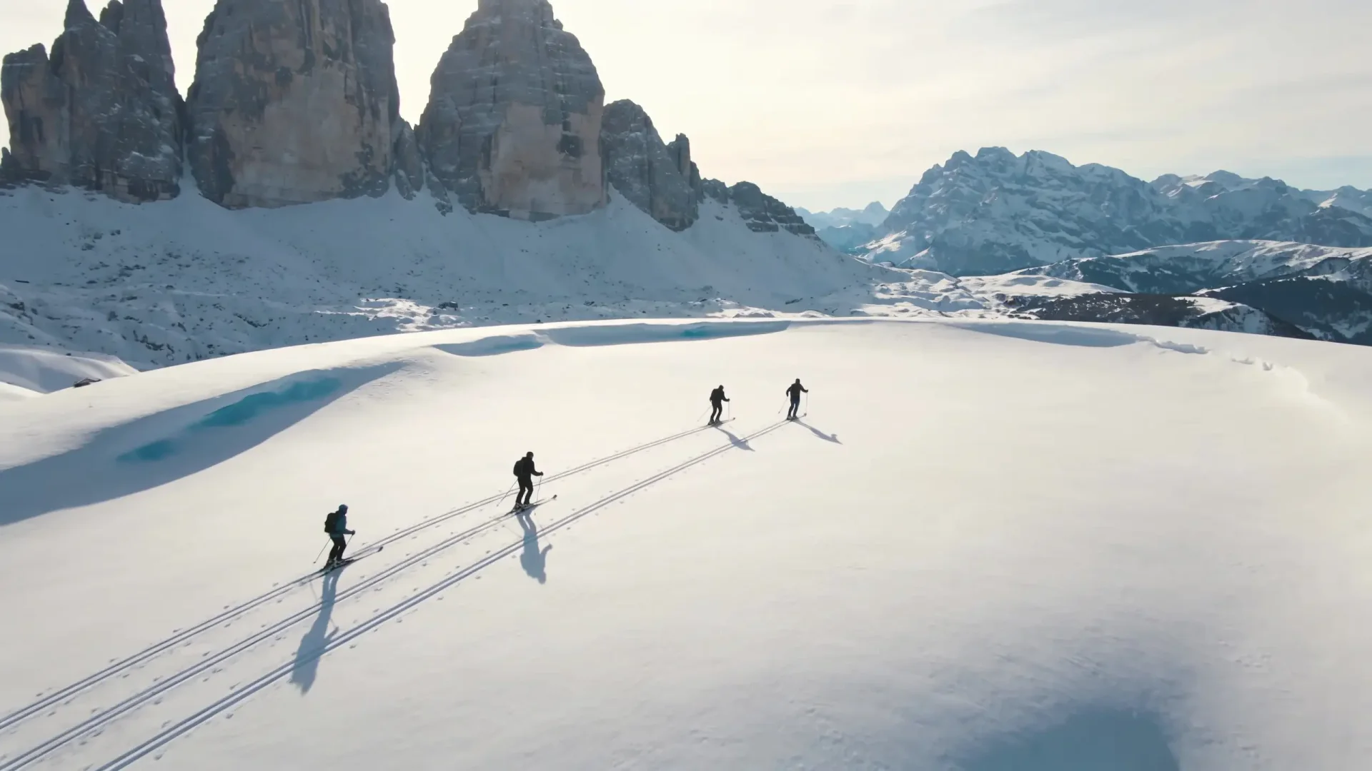 Aerial view of four skiers crossing an untouched alpine snowfield